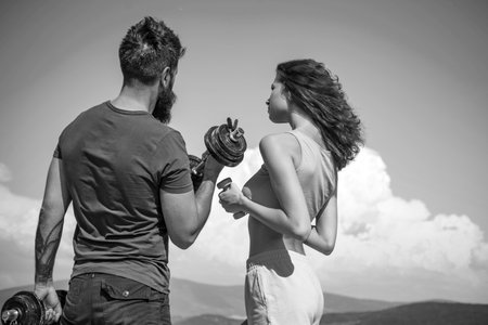Fitness training. Athletic woman and strong bearded man keeping fit with dumbbell training. Sexy couple of athletes having athletic training on nature. Sexi fit woman and hipster doing sport trainingの写真素材