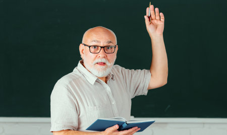 Senior teacher with books and chalkboard. Old smiling professor on lesson at college. Aged male retired teacher.の写真素材