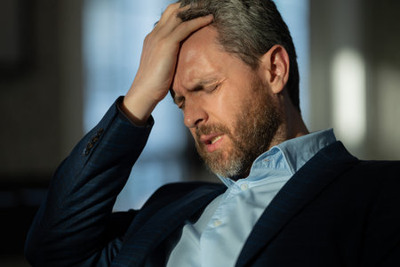 Tired exhausted man suffering from headache. Overworked burnout man feeling migraine head strain. Bored business man has office syndrome. Office worker, manager or freelancer having a headache.の写真素材