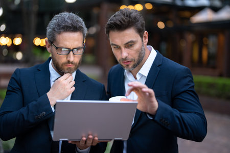 Business men team using laptop outdoor. Businessmen looking laptop with their business success in city background. Two business teams success.の写真素材