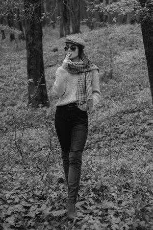 Autumn woman, Brunette girl is smoking a cigarette in the park during autumn. Fashionable model wearing warm brown boots and cap in the forest. Resting from noisy city concept.の写真素材