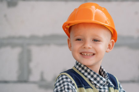 Kid in hard hat holding hammer. Happy smiling little child helping with toy tools on construciton...