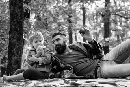Healthy snack. Bite juicy apple. Family picnic. Hipster bearded dad with son spend time in forest. Brutal bearded man and little boy eat apples. Forest picnic hiking. Nature picnic. Vitamin chargeの写真素材