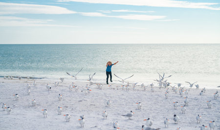 Happy amazed kid running, chasing birds. Child run toward group of birds on sea beach. Kid running...