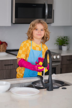 Clean dishes. Cute kid help in washing dishes at kitchen. Kid cleaning of kithen help with housework. Cute child boy housekeeping, child clean house.の写真素材