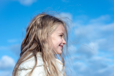 Cute little girl portrait on blue sky. Portrait of kid outdoors. Close-up face child playing...