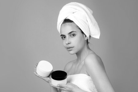 Closeup face of beautiful young woman with cream bottle. Beautiful woman face isolated on studio. Gestures for advertisementの写真素材