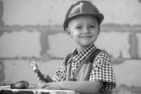 Cute little kid in builder helmet with repair tools on construction site. Child boy in a...