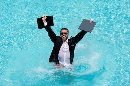 Funny business man relaxing in suit on swimming pool. Summer vacation, business on sea beach. Summer rest, business people concept. Wealthy business man relaxing in swimming pool. Remote work.の写真素材