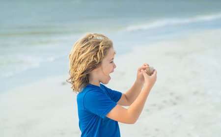 Portrait of little kid holding seashells and dreaming about summer vocation. Cute child playing with shell outdoor on summer beach. Little kid on summer vacations. Summer vacation concept.の写真素材
