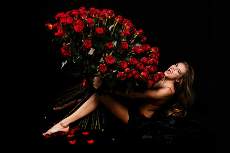 Sensual woman with red lips with red rose, black background. Beautiful sexy woman holding large bouquet of red roses on black background. Valentines day. Holiday birthday day.の写真素材
