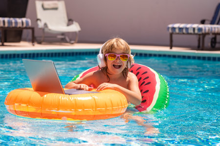 Child sitting in swimming ring in pool and using laptop. Shopping online, freelance concept, summer...