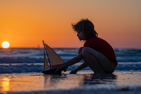 Kid play on the beach on a sunny day. Little sailor play with sailing boat in sea water. Child dreams of travel and adventure. Happy summer holidays concept. Dreams of sea, adventures and travel.の写真素材