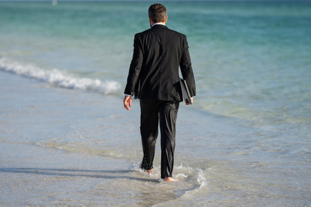 Rear view of back business man in suit in sea water at beach. Summer rest, business people concept. Business man remote on-line working. Dream for summer vacations office workers.の写真素材