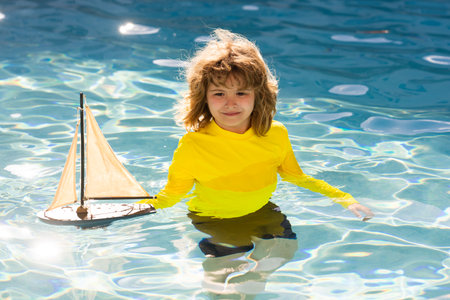 Kid playing with toy sailboat on sea beach at the summer sunset time. Sunset silhouette of child boy dreaming on cruise. Dreaming to travel. kid playing with toy sailing boat. Children day.の写真素材