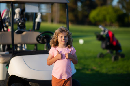 Kid in golf park near golf cart. Child summer vacation. Portrait of kid boy in nature, park or outdoors. Close up face of happy child playing outdoors in summer park.の写真素材