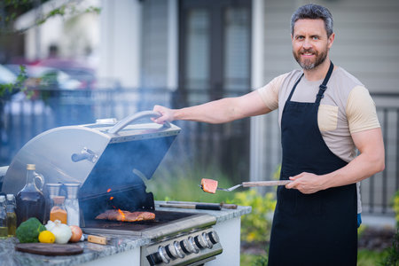 Male chef grilling and barbequing in garden. Barbecue outdoor garden party. Handsome man preparing barbecue meat. Concept of eating and cooking outdoor during summer time.の写真素材