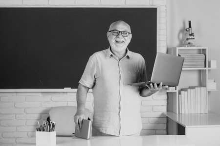 Portrait of mature teacher or tutor professor working at table in college or high school. Elderly education and retired knowledge concept.の写真素材