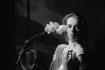 Beautiful woman with flower near the face on black background. Woman with orchid. Cosmetology,...