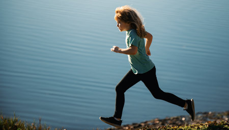 Happy boy run to lake. Child have fun on lake, run by water. Active family lifestyle, kids outdoor water sports. Sporty young child jogging and training outdoor.の写真素材