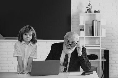 Senior teacher and pupil in classroom. Education concept. Boy elementary school. Old and Young. Grandfather and child learning concept.の写真素材