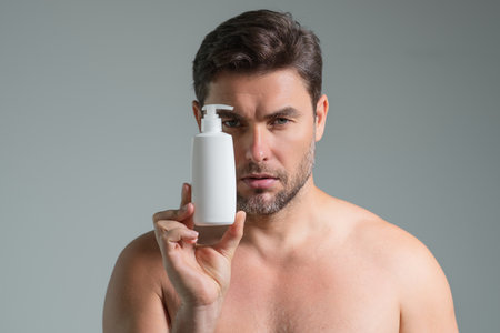 Cosmetics male products. Man hold bottle with dispenser pump for liquid soap, gel or foam, beauty product and cosmetics. Advertising with cosmetics bottle, spa marketing. Beauty concept.の写真素材