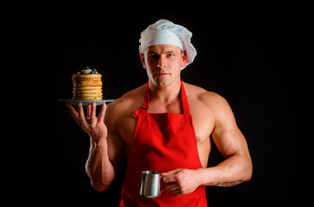 Sexy muscular man in chefs hat with sweet homemade stack of pancakes with syrup. Chef muscle man with apron bake pancakes with berries and maple syrup.の写真素材