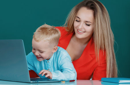 Portrait of schoolkids and teacher talking at school lesson. Mother and son together using computer laptop. Teacher helping elementary school pupils in computer class, learning with laptop.の写真素材