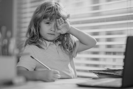 Tired sad school boy while doing homework. Child hold a pencil and draw at home. Schoolboy teen...
