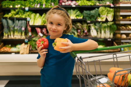 Kid with vegetables and peppers at grocery store. Kid choosing fruits and vegetables during shopping at vegetable supermarket. Little kid going shopping. Healthy food for kids.の写真素材