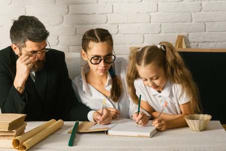 Elementary students with teacher in classroom. Father teaching schoolchild girls. Father and little kids daughters at school. Reading book and writing.の写真素材