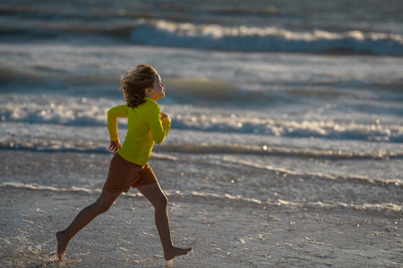 Exited carefree little boy running on wet coast near waving sea on sunny summer day. Kid running at summer beach. Carefree child. Excited child running in the summer sea. Cute kid run on summer sea.の写真素材
