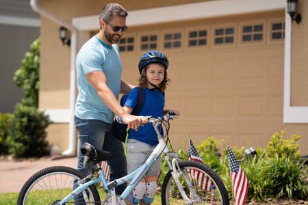 Fathers day. Father teaching son ride a bicycle. Father and son cycling on bike on summer day. Father support child. Fathers love. Sporty kids. Cute boy with dad cycling in summer park outdoor.の写真素材