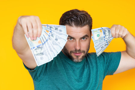 Man hold money on yellow studio isolated background. Rich man with money dollar bills. Successful guy with dollar banknotes. Rich millionaire holding money.の写真素材