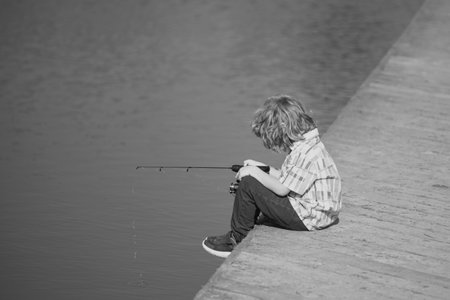 Child boy engaged in fishing hobbies, holds a fishing rod. Summer children lifestyle. Kids fishing on weekend, copy space.の写真素材