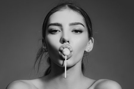 Sensual glamorous attractive lady licking yummy sugary lollypop with red lips. Girl sucks lollipop. Flirting sexy female pop art style. Portrait of sexy woman.の写真素材
