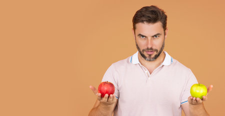 Stomatology concept. Man holding apple on beige studio isolated background. Man eat green apple. Close up portrait of young man with green and red apples. Healthy diet food. Banner, copy space.の写真素材