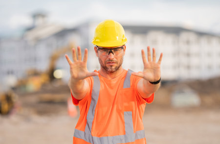 Worker with stop hand gesture. Builder in a hard hat working on a construction project at a site. A...