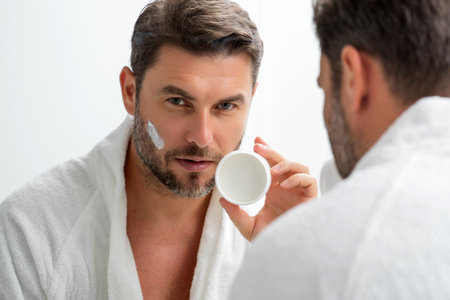 Handsome aged man applying face cream. Beauty routine. Man with perfect skin. Anti-aging and wrinkle cream. Concept of male beauty. Close up face of man applying cream to skin. Skincare and cosmetics.の写真素材