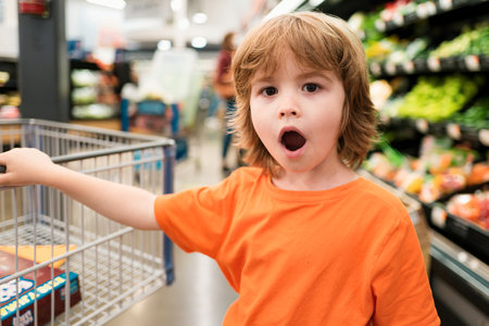Funny shopping. Joyful beautiful child boy in supermarket buys vegetables. Healthy food for children.の写真素材