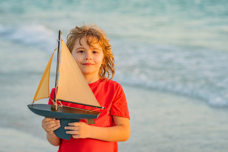Kid play with toy sailing boat. Summer travel, kids holidays. Journey trip lifestyle yachting marine concept. Child playing with toy boat in summer sea. Dream on cruise. Travel, summer holiday.の写真素材