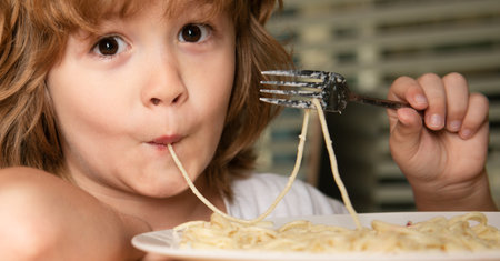 Portrait of a small blond boy eating pasta, spaghetti, closeup. Cute kids face. Positive emotional child.の写真素材