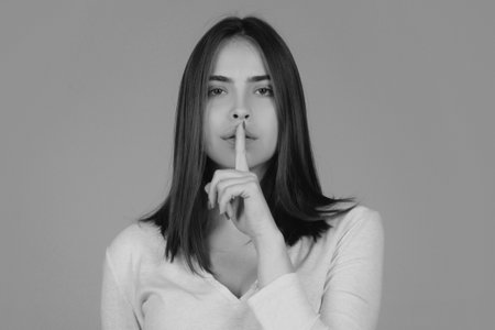 Shh, womens secrets. Woman showing secret sign. Female with finger in mouth. Closeup portrait of young woman is showing a sign of silence with shhh.の写真素材