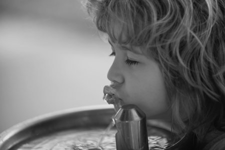 Child drinking water from a water fountain in park.の写真素材
