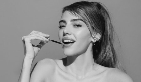 Young woman applies lipstick on lips. Portrait of beautiful glamor model with stylish makeup on the...
