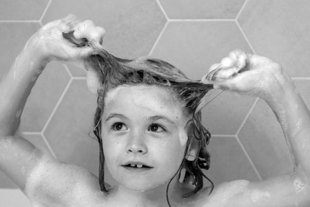 Kid washing hair. Soap on child head. Child face in foam. Kid bathing in a bath with foam. Funny kid face bathed in the bath.の写真素材