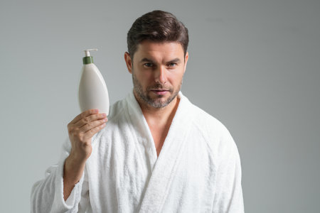 Male model hold bottle with dispenser pump for liquid soap, gel or foam. Facial treatment. Beauty portrait of sexy man cosmetics products isolated on gray studio background, beauty and spa.の写真素材