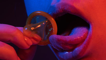 Mouth of a girl with tongue licking a condom. Sexy woman mouth with condoms. Sexy woman with condom in lips, closeup. Erotic concept. Condom in open mouth and sexy lips. Safe sex. Girl using condom.の写真素材