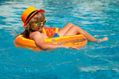 Kid boy swimming in pool play with floating ring. Smiling cute kid in sunglasses swim with inflatable rings in pool in summer day. Child relax with pool ring in beach sea water.の写真素材