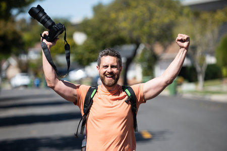 Man excited photographer with a large professional camera. Portrait of photographer with camera outdoor. Tourist photographer.の写真素材